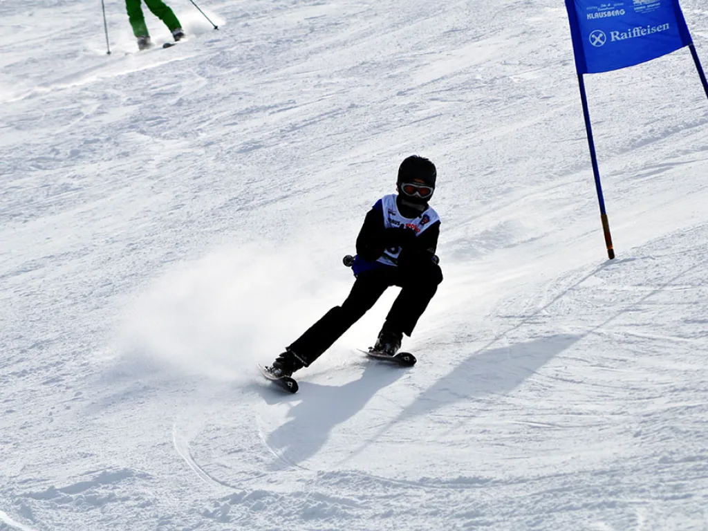 Snowboarder mit aufstiebendem Schnee vor dem blauen Tor.